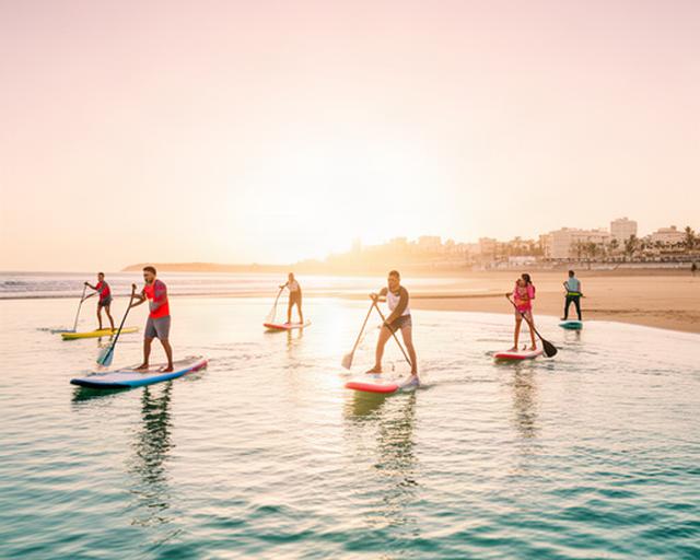 Grupo practicando paddle surf en una playa tranquila de Cádiz al amanecer